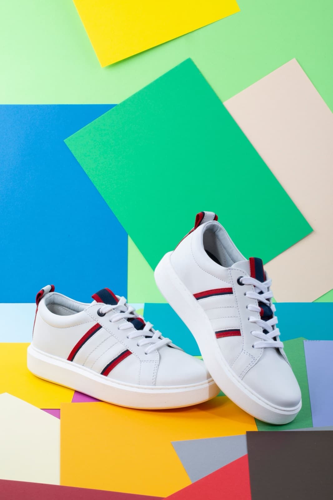 White leather sneakers with red and navy stripes on a colourful paper background