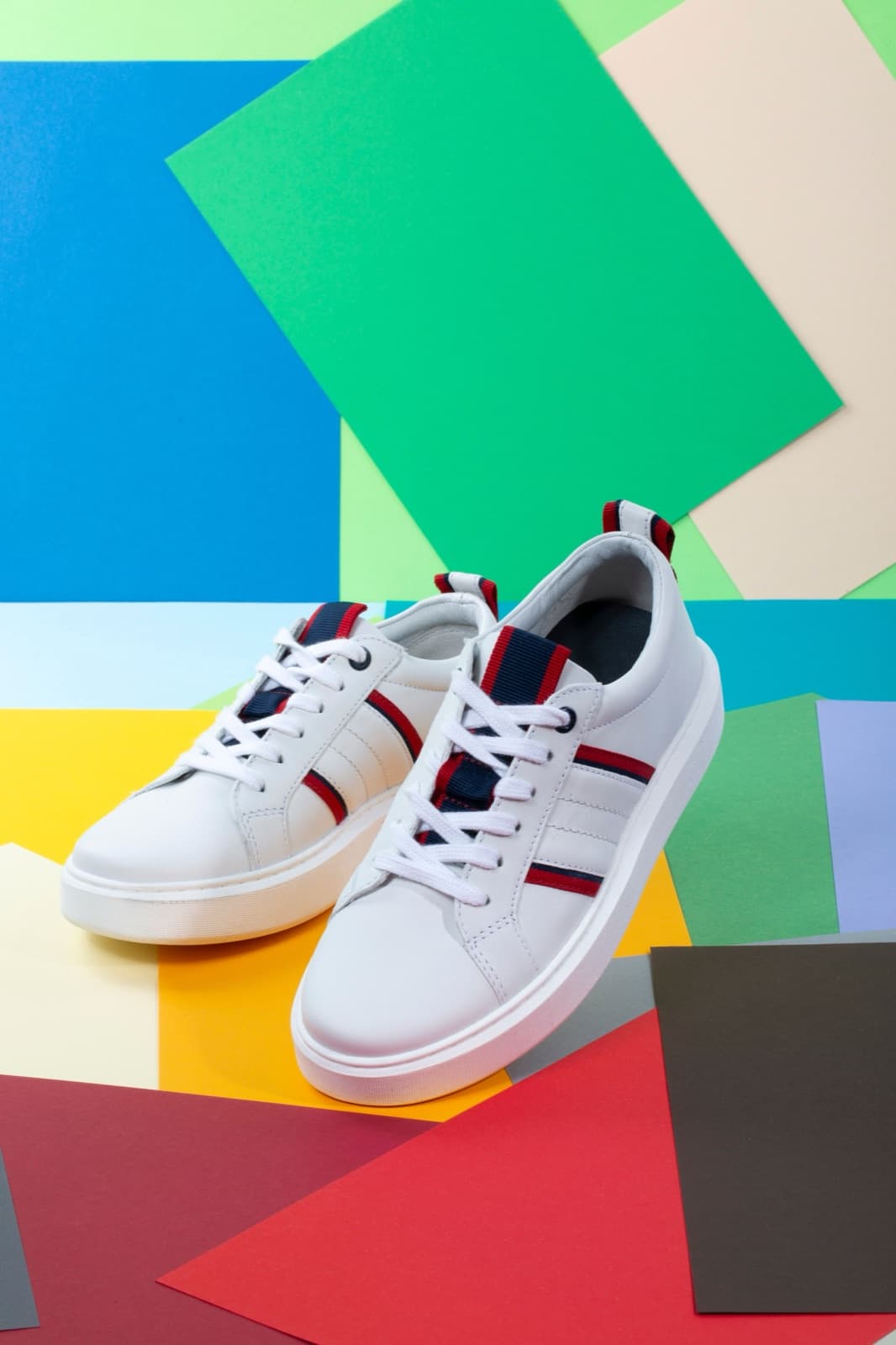 One white striped sneaker angled towards the camera on a geometric background