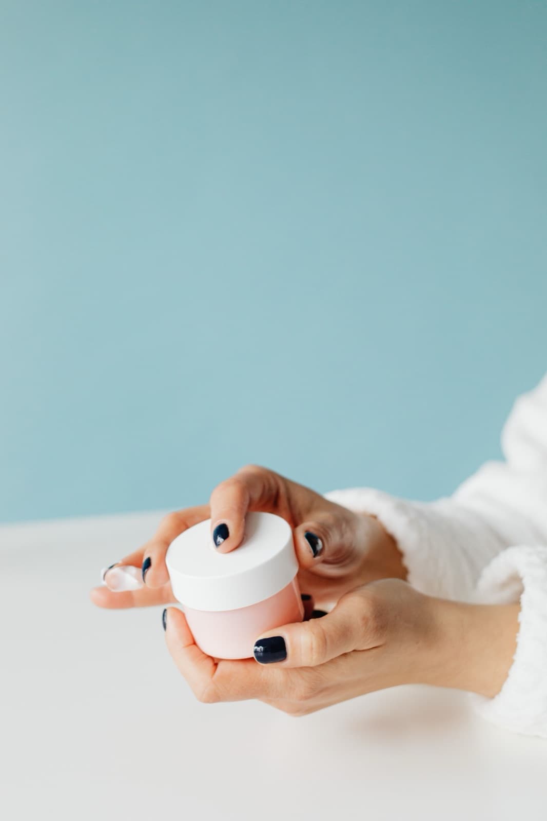 Two hands holding the open pink moisturiser jar