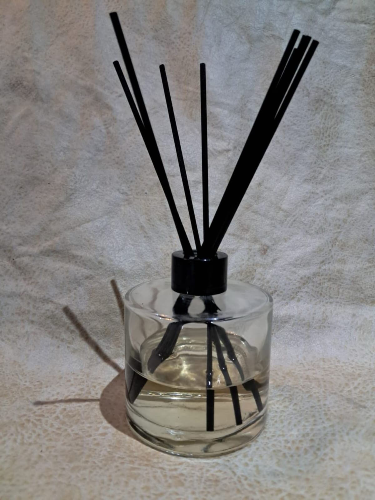 Clear glass reed diffuser with black reeds on a grey linen background